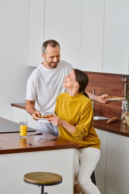 smiling man serving tasty breakfast near laughing wife in kitchen, morning of child-free couple clipart