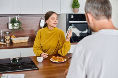 Kocasıyla kahvaltı ederken akıllı telefondan haber okuyan gülümseyen kadın, çocuksuz bir çift.