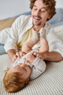 Kıvırcık saçlı mutlu baba, bebeğiyle oynarken yatakta birlikte, masum.