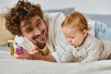 Bekar bir baba kucağında renkli çıngıraklar, yatak odasında erkek bebek, baba ve oğul arasında bir bağ.