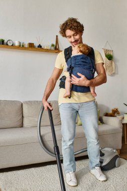 Mutlu baba ve bebek taşıyıcı çocuk oturma odasını, temizliği ve ev işlerini süpürüyor.