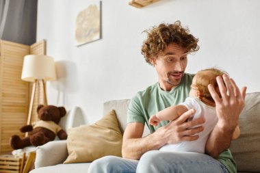 Sakallı neşeli bir baba, rahat bir oturma odasında küçük oğluna bakıyor, babalık ve neşe içinde