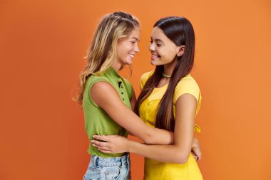 Neşeli, sevimli, günlük giysiler içinde genç kızlar kucaklaşıp gülümsüyorlar, dostluk günü.