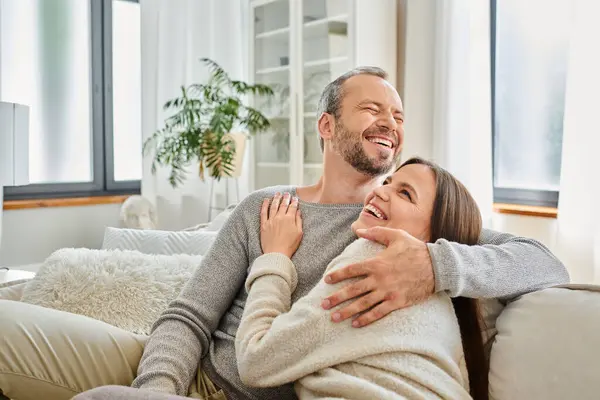 stock image excited child-free couple embracing and laughing on couch in modern living room, calm lifestyle