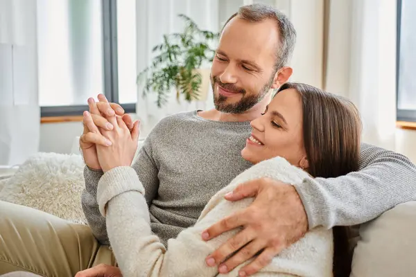 stock image smiling child-free couple holding hands and embracing on couch in living room, warm relationship