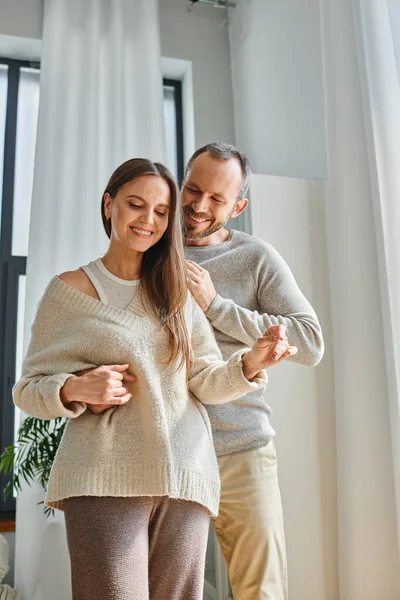 smiling man hugging happy wife in modern living room at cozy home, child-free modern lifestyle