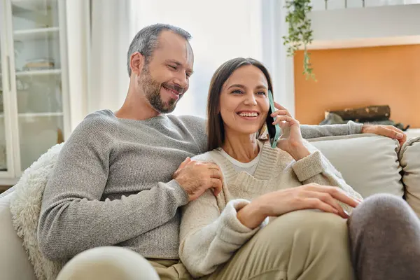 Oturma odasındaki akıllı telefon koltuğunda gülümseyen koca ve çocuksuz bir çiftin yanında konuşan neşeli bir kadın.