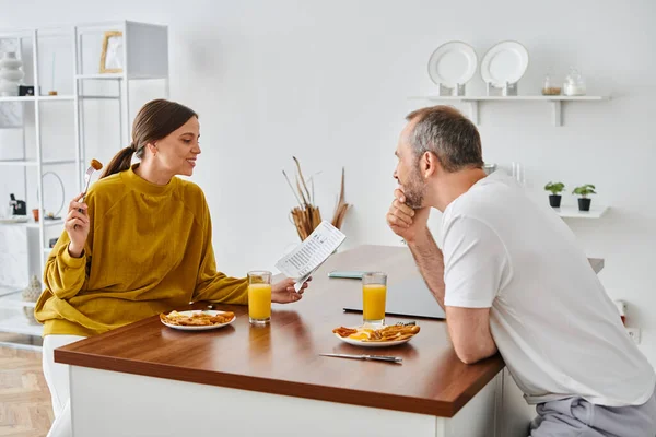 stock image smiling woman reading newspaper during breakfast with husband in modern kitchen, child-free couple