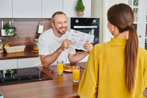 stock image cheerful man showing newspaper to wife during breakfast in modern kitchen, child-free lifestyle