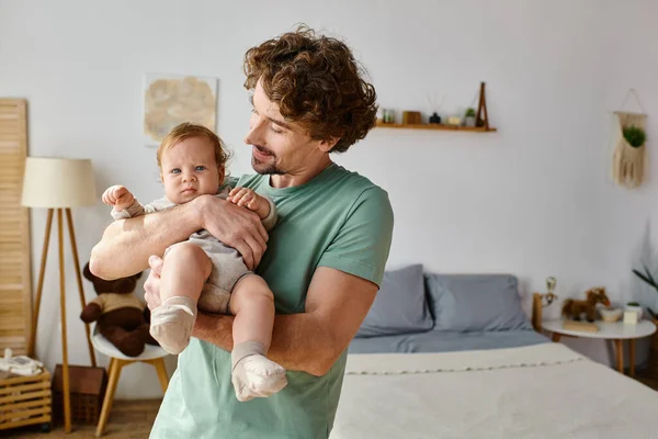 カーリー ヘアで幸せな父親は 自宅で居心地の良い寝室で赤ちゃんの息子を抱えている — ストック写真