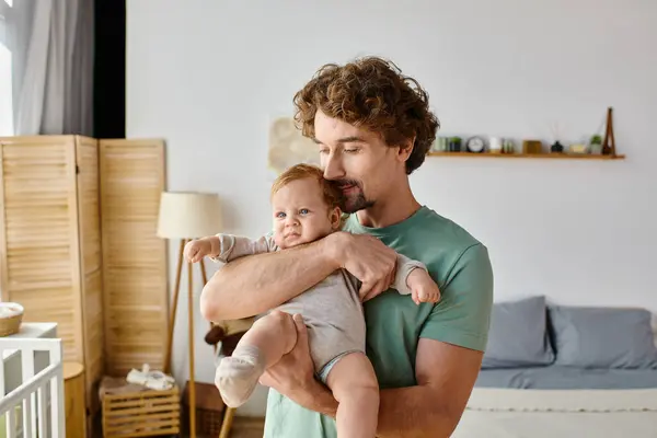 カーリー ヘアと陽気な父親は 自宅で居心地の良い寝室で赤ちゃんの男の子を抱えています 父親時代 — ストック写真