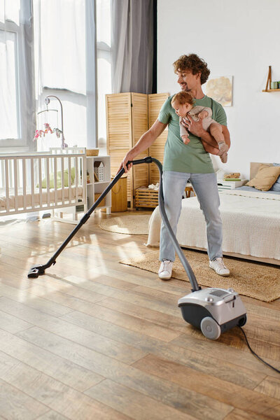 кудрявый отец многозадачная работа по дому и уходу за детьми, мужчина пылесосит спальню с младенцем сына на руках