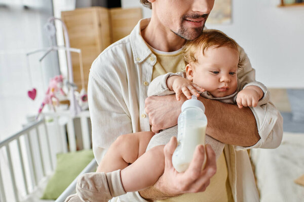 cropped father attentively feeding his infant son with milk in baby bottle, fatherhood and care