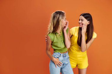 joyous pretty teens in bright attires smiling at each other on orange backdrop, friendship day clipart