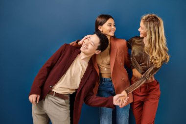 Moda kıyafetleri içinde neşeli çok kültürlü arkadaşlar koyu mavi arka planda poz verirken eğleniyorlar.