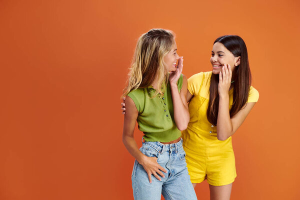 joyous pretty teens in bright attires smiling at each other on orange backdrop, friendship day