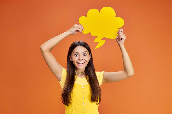 cheerful adolescent girl in everyday outfit with thought bubble looking at camera on orange backdrop