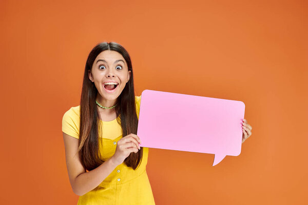 jolly pretty adolescent girl in vibrant clothing holding speech bubble and looking at camera