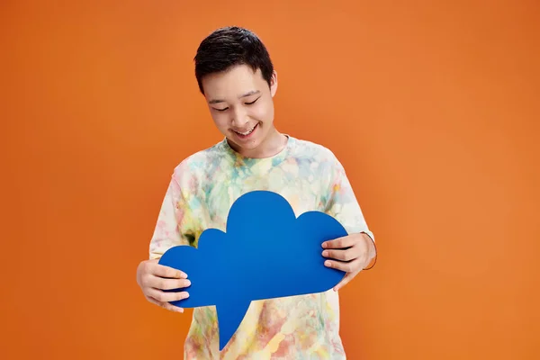 stock image joyful adolescent asian boy in casual attire smiling happily and holding blue thought bubble