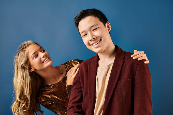 jolly asian boy looking at camera while his blonde joyful friend smiling at him on blue background