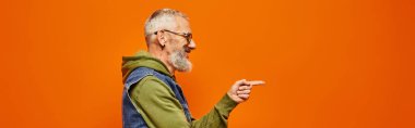 handsome joyful mature man in vibrant attire posing in profile and pointing in front of him, banner clipart