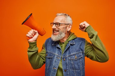 cheerful handsome mature male model in vibrant outfit posing with megaphone and looking away clipart