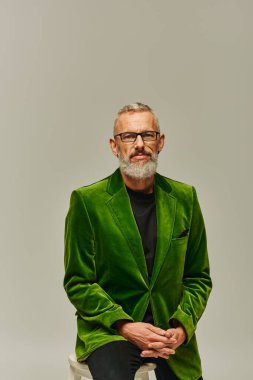 Gözlüklü, gri sakallı, yeşil ceketli, uzun sandalyede oturan çekici, olgun bir erkek model.