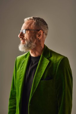 Yeşil parlak ceketli, gri sakallı ve gözlüklü neşeli ve yakışıklı bir erkek model.