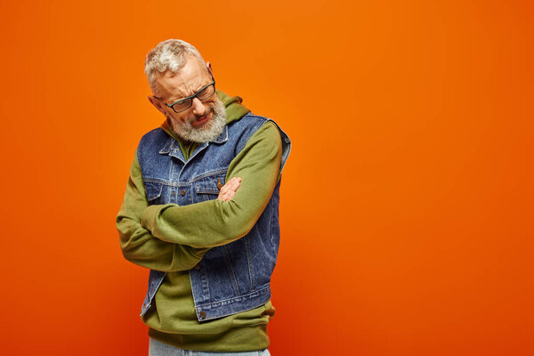 красивый зрелый мужчина в ярком одеянии с скрещенными руками на груди на оранжевом фоне