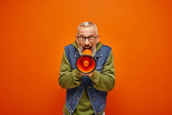 фанки привлекательный зрелый мужчина в стильном джинсовом жилете говорить в мегафон и смотреть в камеру
