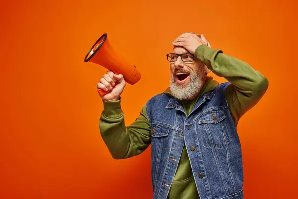 surprised jolly mature male model in vibrant stylish outfit posing with megaphone with hand on head