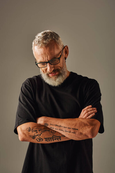 веселый зрелый мужчина модель в черной футболке позирует с руками скрещенными на груди и глядя вниз