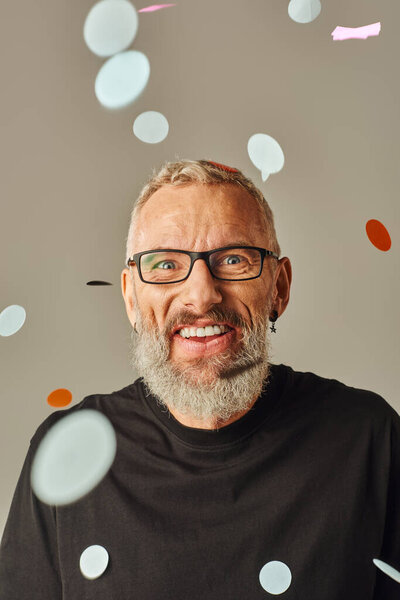 веселый красивый мужчина модель в черной футболке с очками улыбаясь в камеру под конфетти дождь