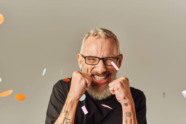 веселый фанки зрелый мужчина в черной футболке с очками, смотрящий в камеру под дождём конфетти