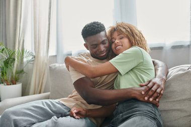 Mutlu Afro-Amerikan kadın diş teli takmış kanepede otururken sevgilisini kucaklıyor, kaliteli zaman geçiriyor.