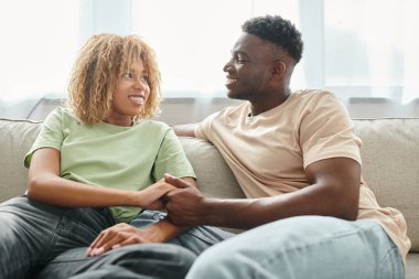 Tender moment between african american couple at home, man and woman holding hands in living room clipart