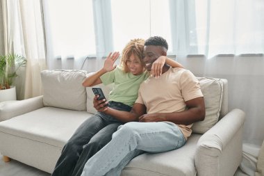 Mutlu Afro-Amerikan çifti birlikte kanepede otururken akıllı telefondan sohbet ediyor.
