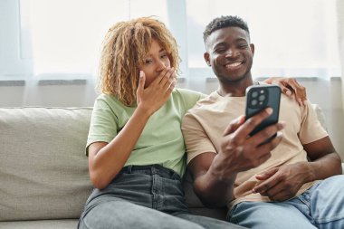 happy african american couple laughing while video chatting on a smartphone at home, communication clipart