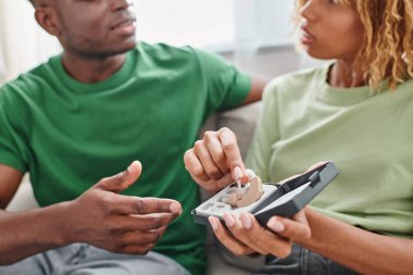 cropped shot of african american woman holding box with hearing aid medical device near man clipart