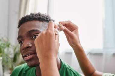 african american man smiling as his girlfriend assists him with hearing aid, medical equipment clipart