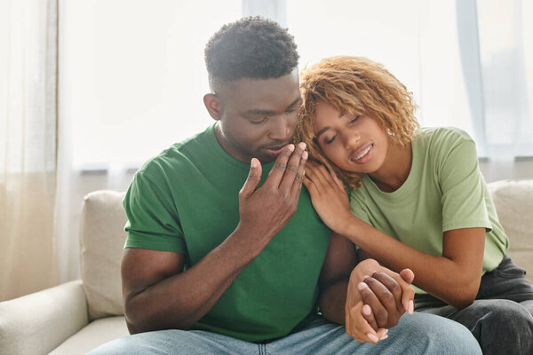 young african american couple holding hands while sitting together on sofa, quality time