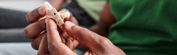 hearing aid in hands on black man, african american person holding medical device, banner