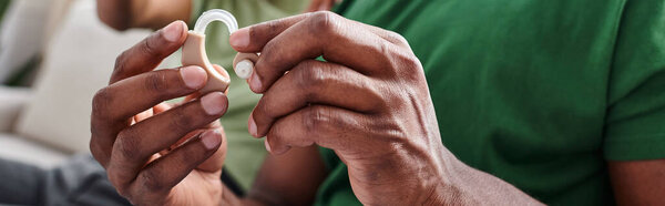 cropped banner of hearing aid in hands on black man, african american person holding medical device
