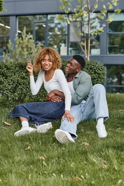 stock image excited african american couple hugging and sitting together on green grass, happiness