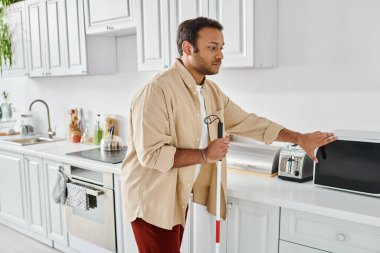 attractive indian man with visual impairment wearing cozy homewear and preparing food, disabled clipart