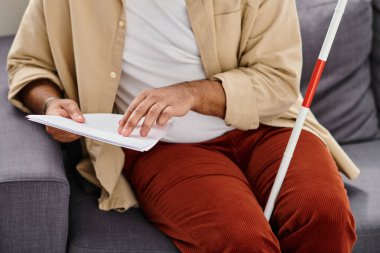 Kanepede oturmuş, körler alfabesi kodları okuyan, gündelik kıyafetli Hintli kör adam görüntüsü.