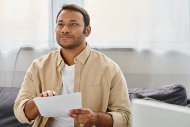 attractive indian man with blindness in cozy clothing sitting on sofa and reading braille code clipart