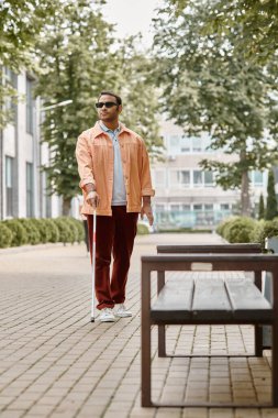 Parkta yürüyen turuncu ceketli, gözlüklü ve bastonlu çekici Hintli kör adam.