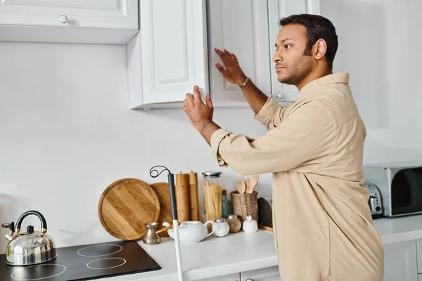 stock image handsome indian disabled man in casual attire with walking stick reaching products on kitchen