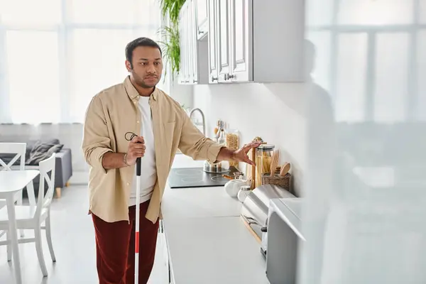 stock image good looking disabled indian man in homewear holding walking stick while preparing food, blind